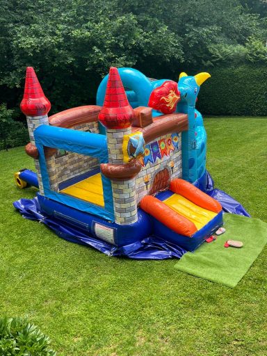 Hüpfburg Drachenland mit Rutsche oben Luftburg mit Burgen, Rutsche und buntem Design im Garten.