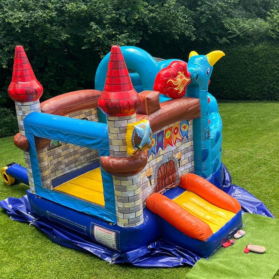 Bunte Hüpfburg mit Türmen und Rutsche auf einer Wiese.