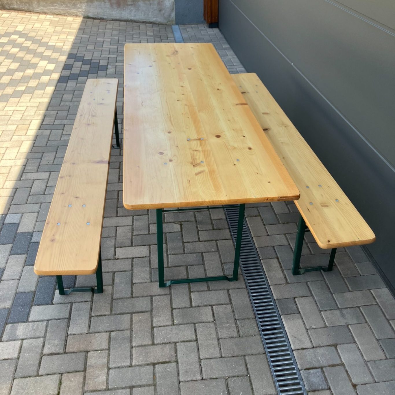 Holztisch mit zwei Bänken, auf einem gepflasterten Boden.